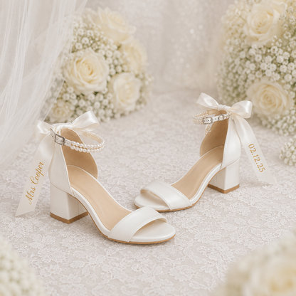 White wedding shoes with ribbons on a soft white background with flowers.