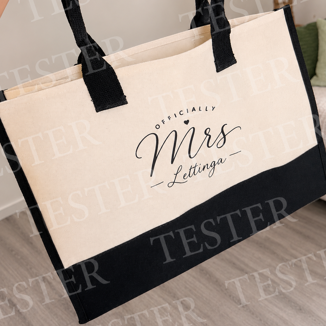 A canvas tote bag with a cream-colored upper section and a black bottom band, featuring black handles. The front is printed with the text 'OFFICIALLY Mrs Lettinga' in black script.