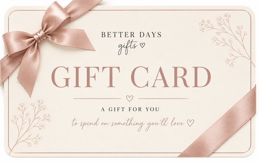 A square gift card design with a pale blush background, a large satin ribbon bow in the upper left, and a diagonal ribbon strip in the lower right. The card reads 'BETTER DAYS gifts' and 'GIFT CARD' with decorative floral line art in the corners.