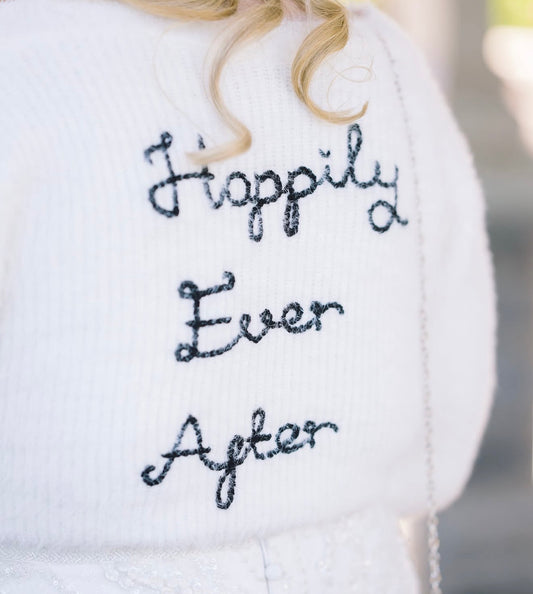 White fluffy cardigan with 'Happily Ever After' embroidery on a blurred background