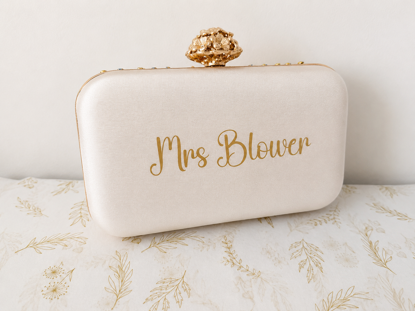 White clutch bag with 'Mrs Blower' text on a floral surface
