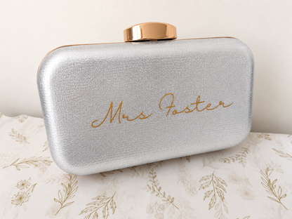 Silver clutch bag with 'Mrs. Foster' engraving on a floral-patterned surface