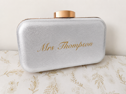 Silver clutch bag with 'Mrs Thompson' engraving on a floral-patterned surface