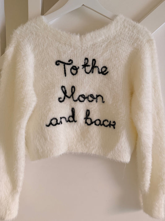 White fluffy sweater with 'To the Moon and back' text on a hanger.